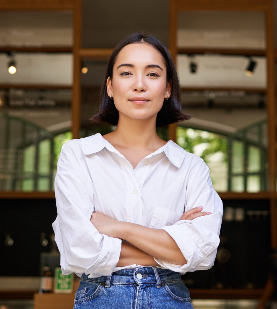 smiling young female manager, cafe owner cross arms on chest, looking confident, standing in front of restaurant