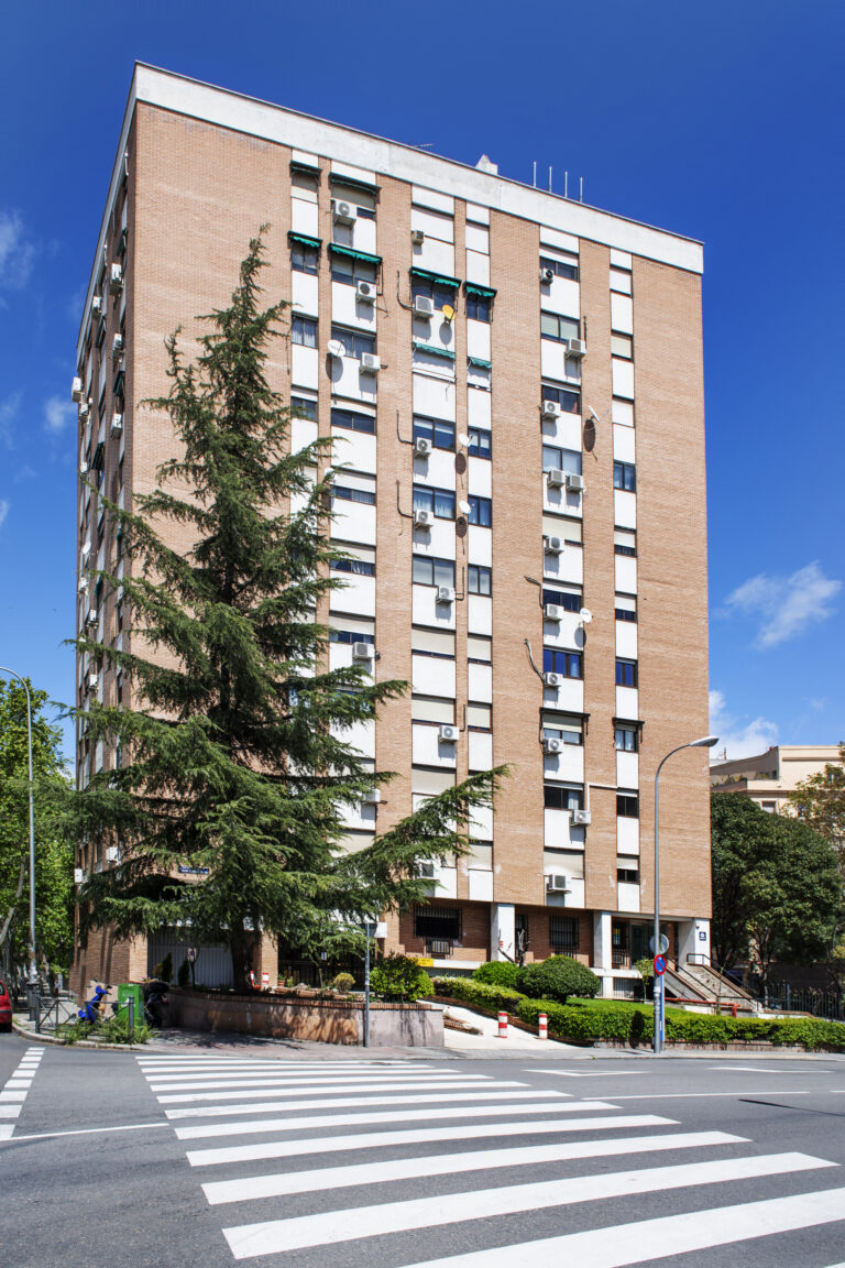 facade of a building with gardens, trees, a black metal portal a
